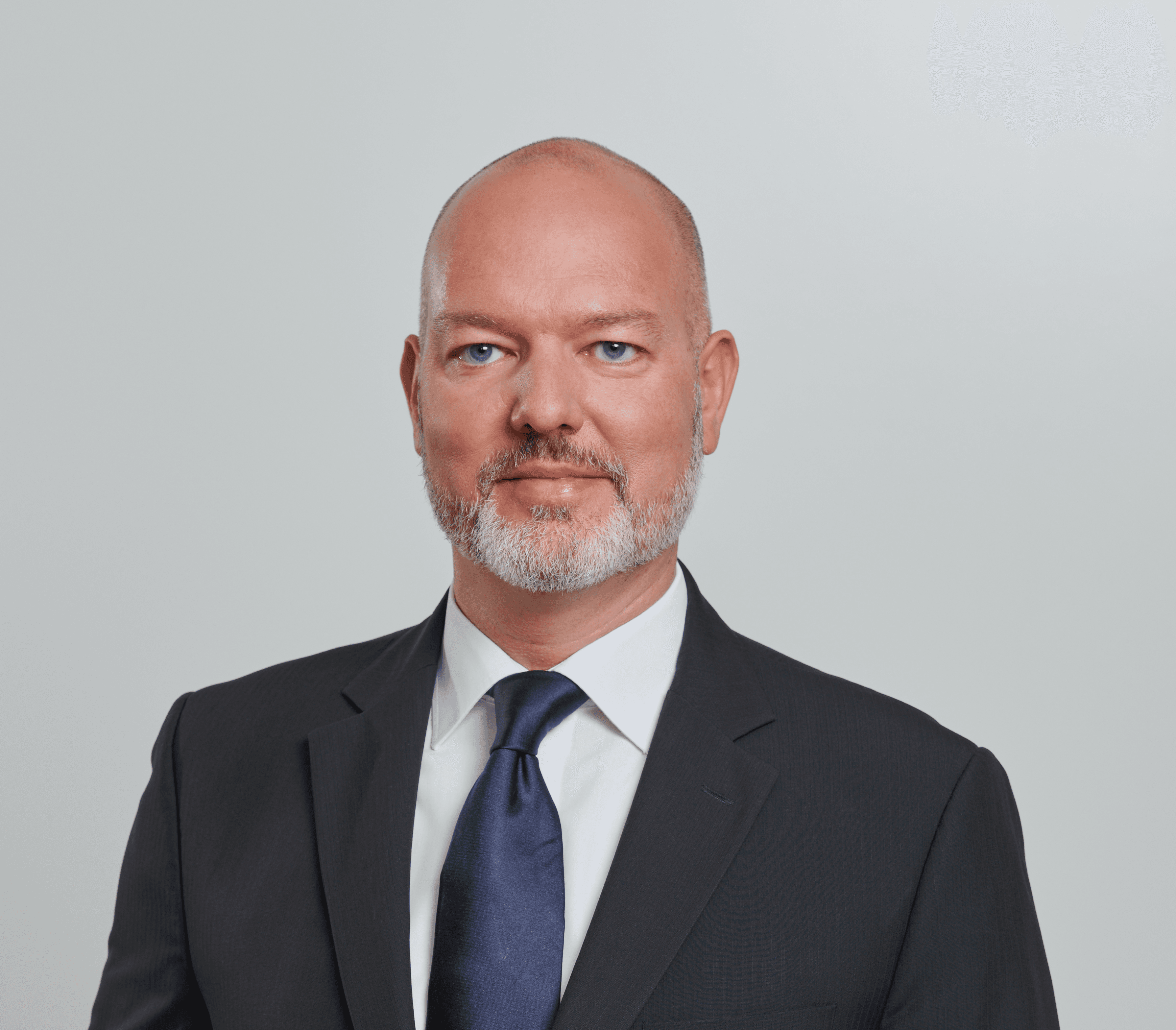 Porträt eines Mannes im schwarzen Anzug mit weißem Hemd und dunkelblauer Krawatte.